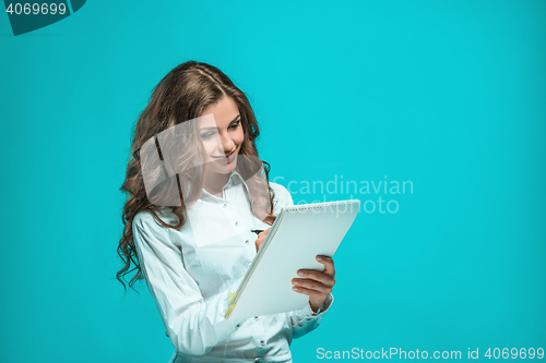 Image of The smiling young business woman with pen and tablet for notes on blue background