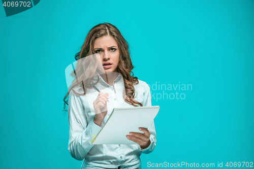 Image of The thoughtful young business woman with pen and tablet for notes on blue background