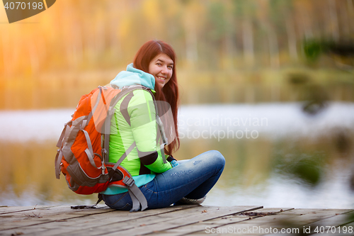 Image of Smiling brunette sitting with backpack on bridge
