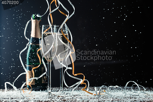 Image of Champagne bottle, glasses on table covered snow and cascading ribbons