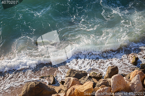 Image of Small waves, sea foam and coastal rocks on sunny day