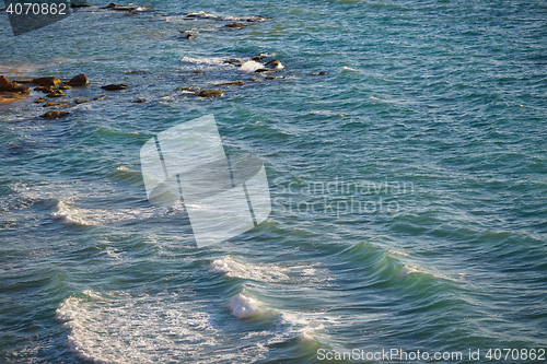 Image of Turquoise sea and light waves lapping protruding stones