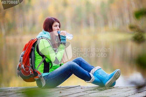 Image of Young brunette drinking water from bottle at pond