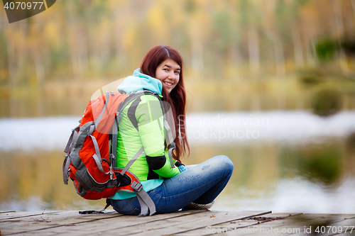 Image of Cheerful brunette sitting with backpack at lake