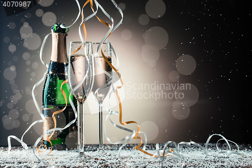 Image of Champagne bottle and two wineglasses on table covered snow