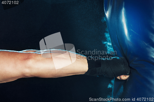 Image of Male boxer boxing in punching bag with dramatic edgy lighting in a dark studio