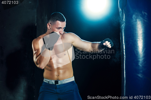 Image of Male boxer boxing in punching bag with dramatic edgy lighting in a dark studio