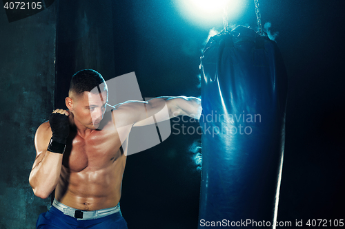 Image of Male boxer boxing in punching bag with dramatic edgy lighting in a dark studio