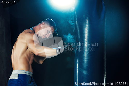 Image of Male boxer boxing in punching bag with dramatic edgy lighting in a dark studio