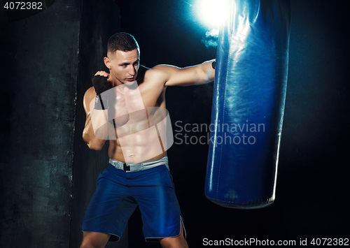 Image of Male boxer boxing in punching bag with dramatic edgy lighting in a dark studio