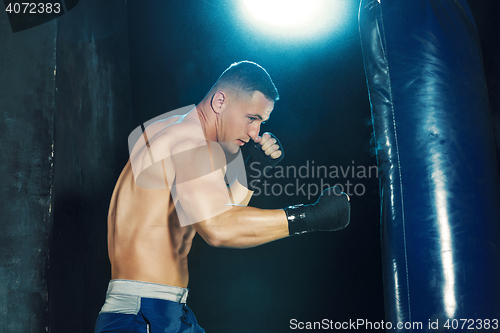 Image of Male boxer boxing in punching bag with dramatic edgy lighting in a dark studio