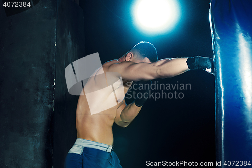 Image of Male boxer boxing in punching bag with dramatic edgy lighting in a dark studio