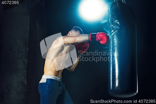 Image of Male boxer boxing in punching bag with dramatic edgy lighting in a dark studio
