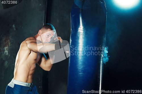 Image of Male boxer boxing in punching bag with dramatic edgy lighting in a dark studio