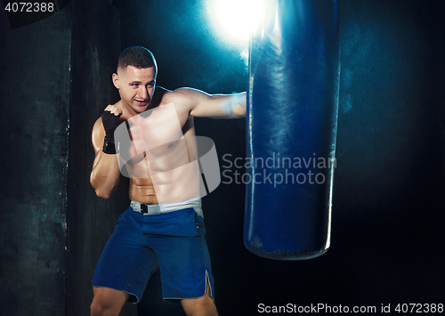 Image of Male boxer boxing in punching bag with dramatic edgy lighting in a dark studio