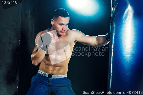 Image of Male boxer boxing in punching bag with dramatic edgy lighting in a dark studio