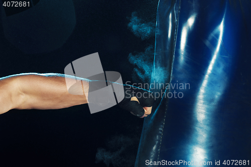 Image of Male boxer boxing in punching bag with dramatic edgy lighting in a dark studio