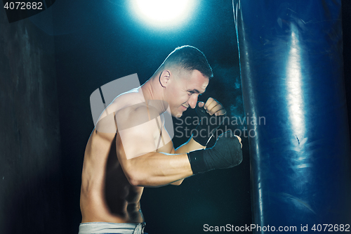 Image of Male boxer boxing in punching bag with dramatic edgy lighting in a dark studio