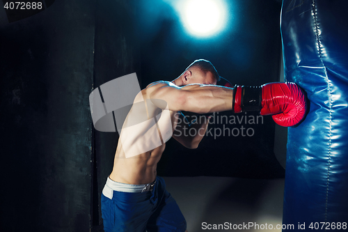 Image of Male boxer boxing in punching bag with dramatic edgy lighting in a dark studio