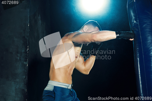 Image of Male boxer boxing in punching bag with dramatic edgy lighting in a dark studio