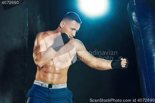 Image of Male boxer boxing in punching bag with dramatic edgy lighting in a dark studio