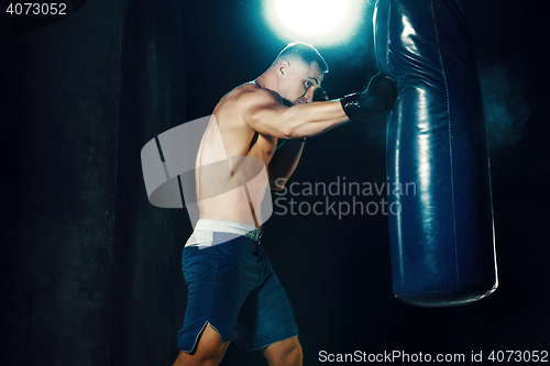 Image of Male boxer boxing in punching bag with dramatic edgy lighting in a dark studio