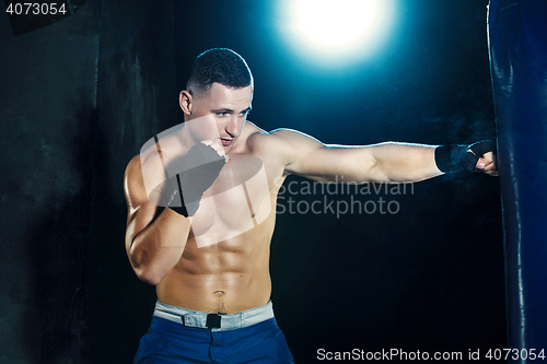 Image of Male boxer boxing in punching bag with dramatic edgy lighting in a dark studio