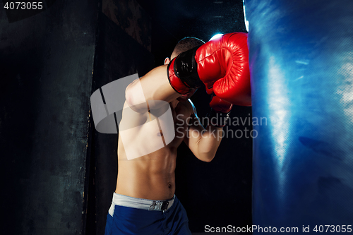 Image of Male boxer boxing in punching bag with dramatic edgy lighting in a dark studio