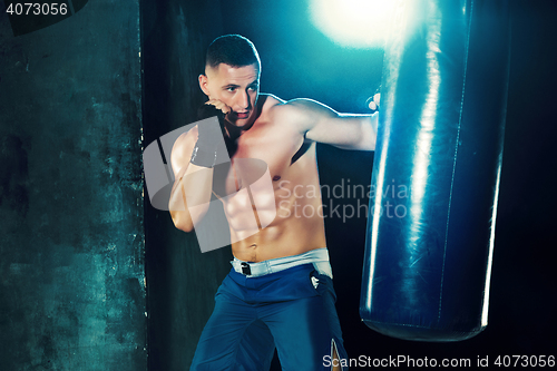 Image of Male boxer boxing in punching bag with dramatic edgy lighting in a dark studio