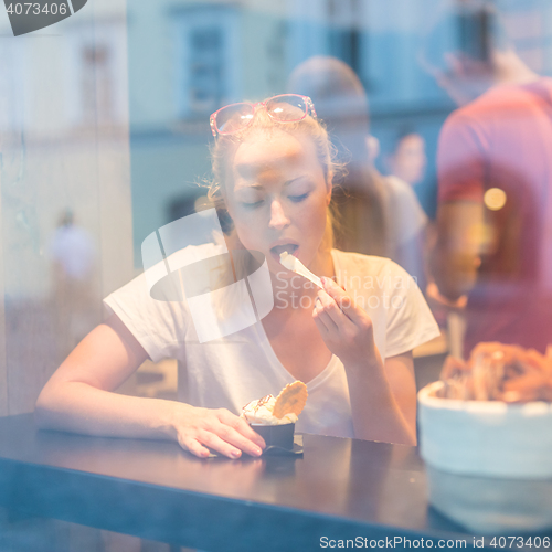 Image of Young pretty woman eating icecream in gelateria.