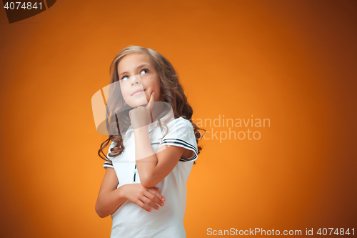 Image of The cute thoughtful little girl on orange background