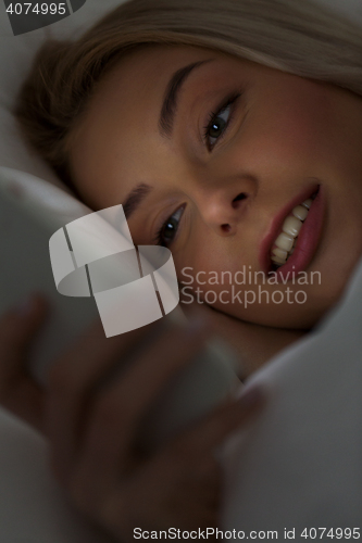 Image of young woman with smartphone in bed at night