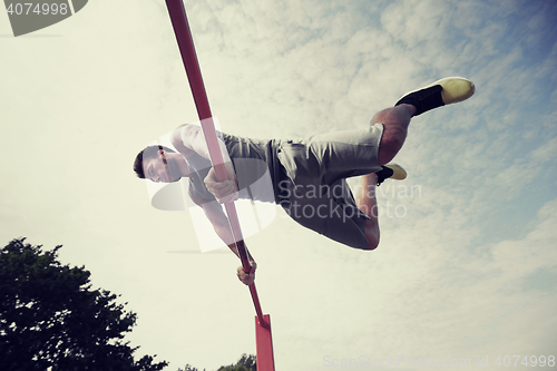 Image of young man exercising on horizontal bar outdoors