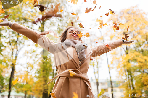 Image of happy woman having fun with leaves in autumn park