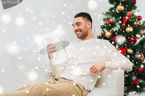 Image of smiling man with smartphone at home for christmas