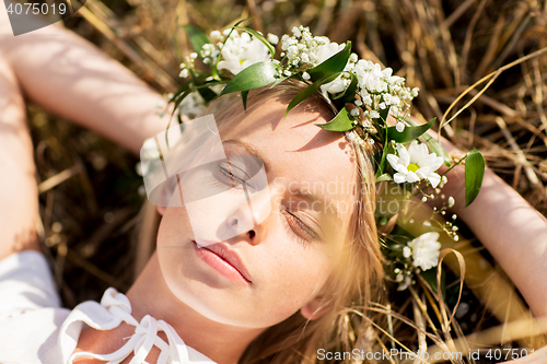 Image of happy woman in wreath of flowers lying on straw