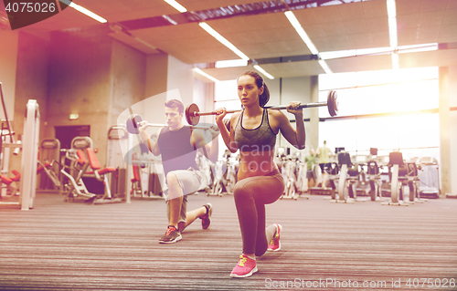 Image of young man and woman training with barbell in gym