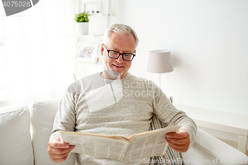 Image of senior man in glasses reading newspaper at home