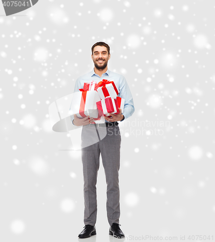 Image of happy young man holding christmas gifts over snow