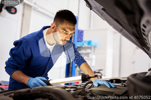 Image of mechanic man with lamp repairing car at workshop