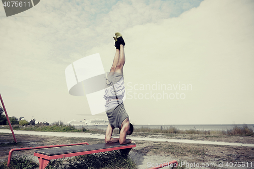 Image of young man exercising on bench outdoors