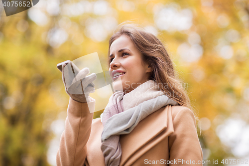 Image of woman recording voice on smartphone in autumn park