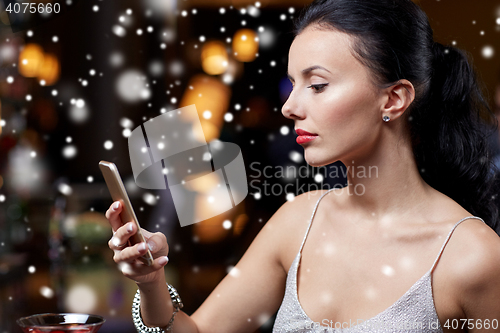 Image of young woman with smartphone at night club or bar