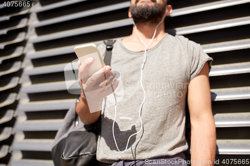Image of man with earphones, smartphone and bag on street