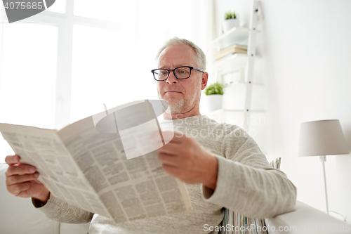 Image of senior man in glasses reading newspaper at home