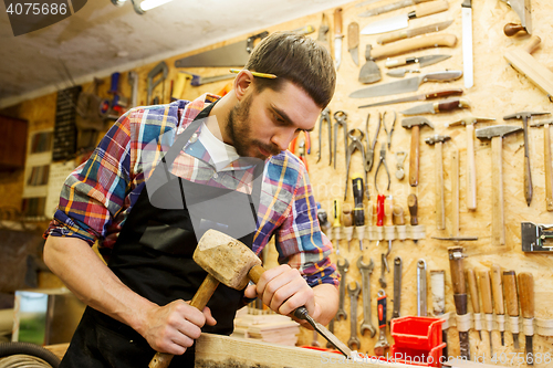 Image of carpenter with wood, hammer and chisel at workshop