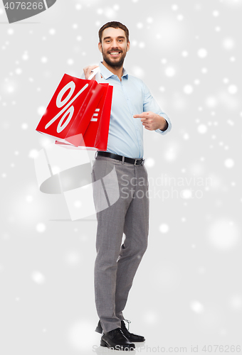 Image of smiling man with red shopping bags over snow