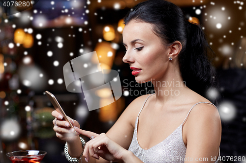 Image of young woman with smartphone at night club or bar
