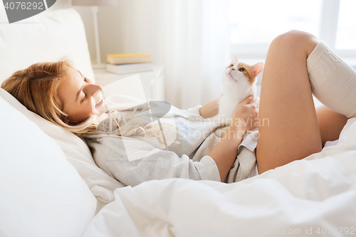 Image of happy young woman with cat in bed at home