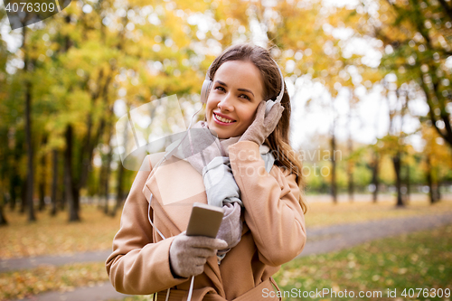 Image of woman with smartphone and earphones in autumn park